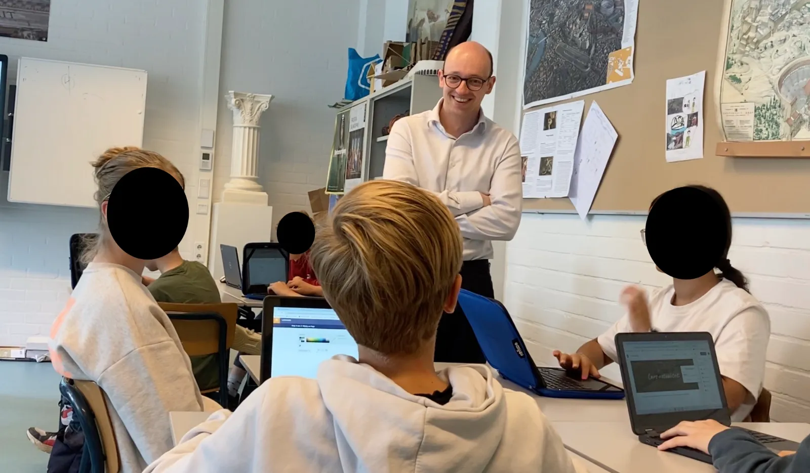 Jan Noordman geeft les en praat met leerlingen in een klas; gezichten van leerlingen zijn afgeschermd